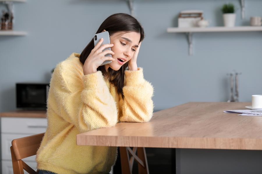 A worried woman on the phone at her kitchen table